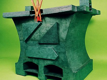 Objet en carton en forme d'enclume en matériau vert, avec des éléments géométriques et des élastiques.